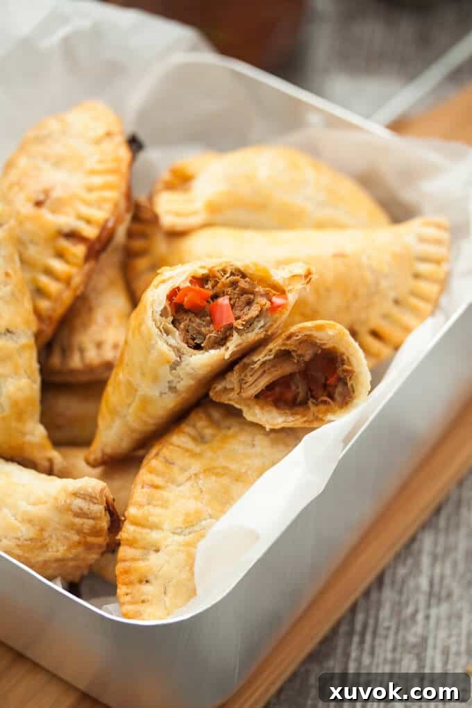 A delicious pulled pork empanada torn in half to reveal its rich, savory filling and the flaky texture of the pastry, placed on a wooden board.