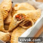 An empanada broken in half to clearly display the rich, savory pulled pork filling and the perfectly flaky pastry layers, tempting viewers to try this delicious dish.