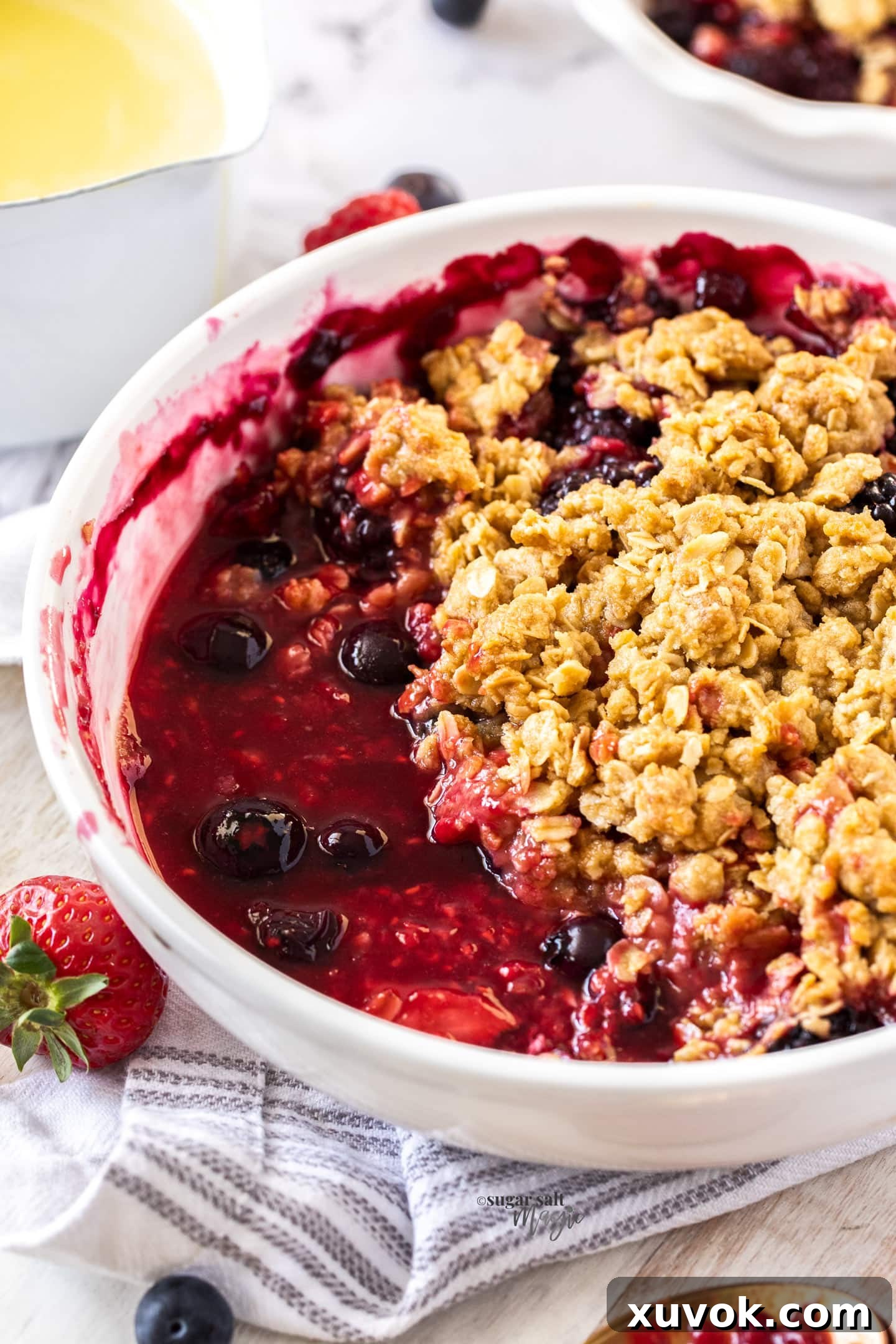 A white pie dish filled with a bubbling mixed berry filling and a golden-brown crumble topping, ready to be served.