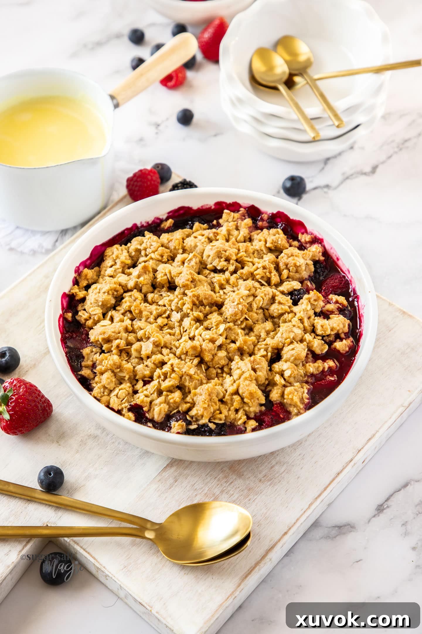 A white pie dish showcasing the mixed berry crumble before baking, with the fruit peeking through the topping.