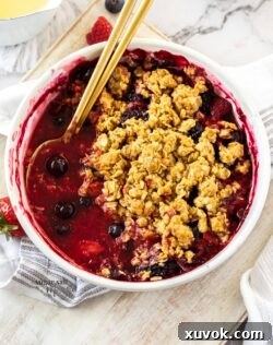 Top down view of a mixed berry crumble with gold spoons in it.