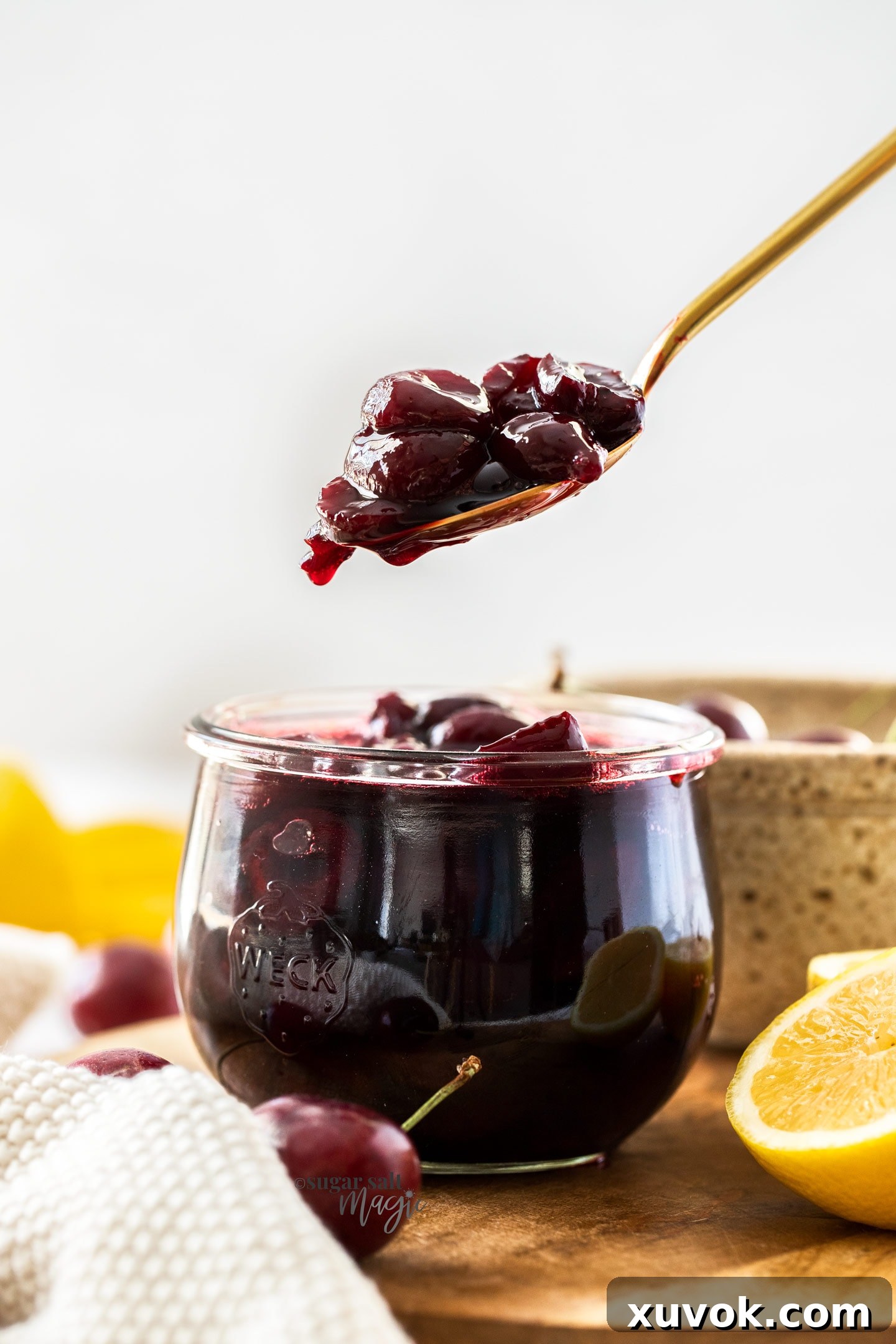 A gold spoon filled with cherry compote hovering over a jar full of it