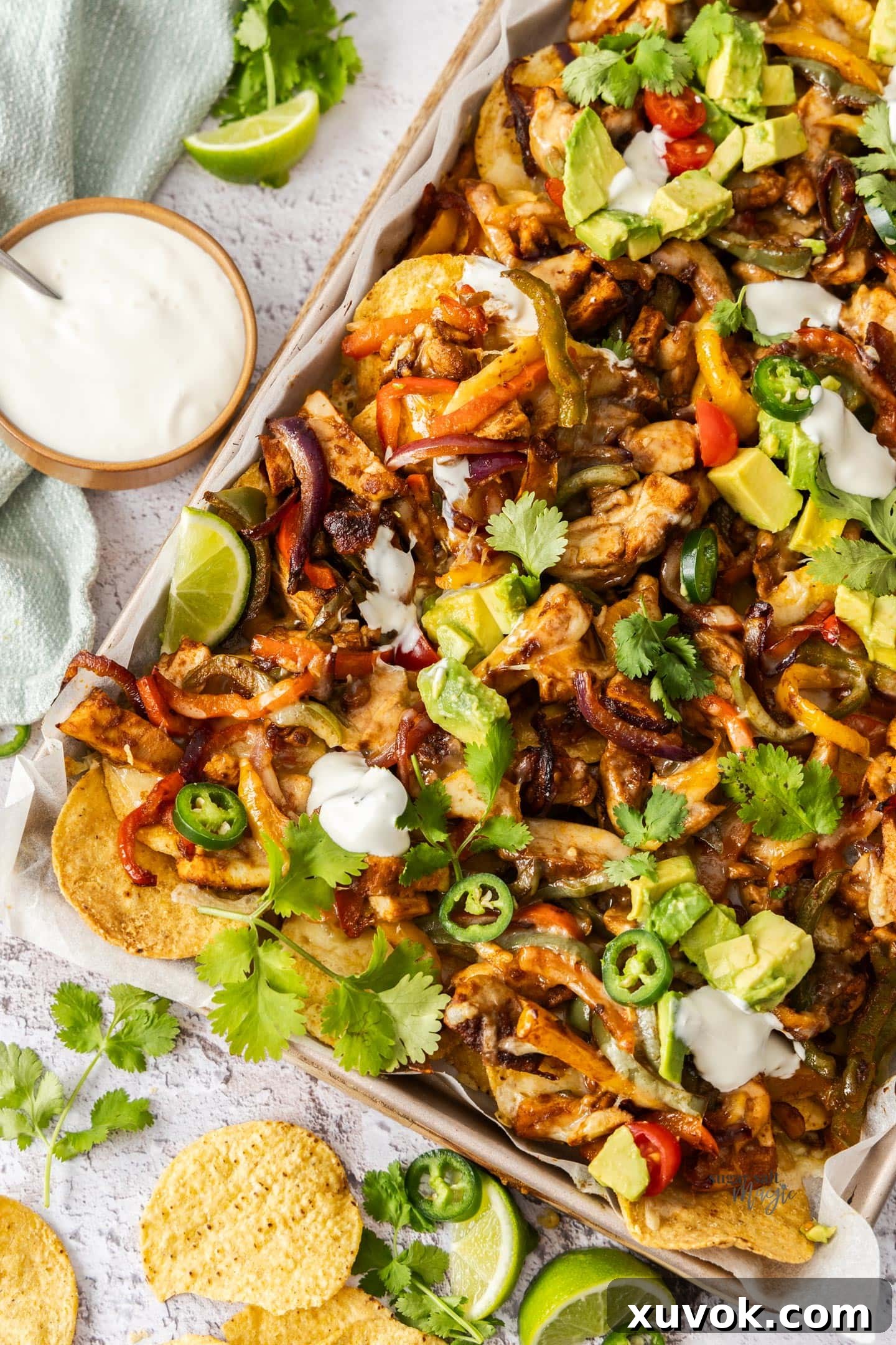 Top down view of chicken fajita nachos on a baking tray, garnished with fresh cilantro and avocado slices.