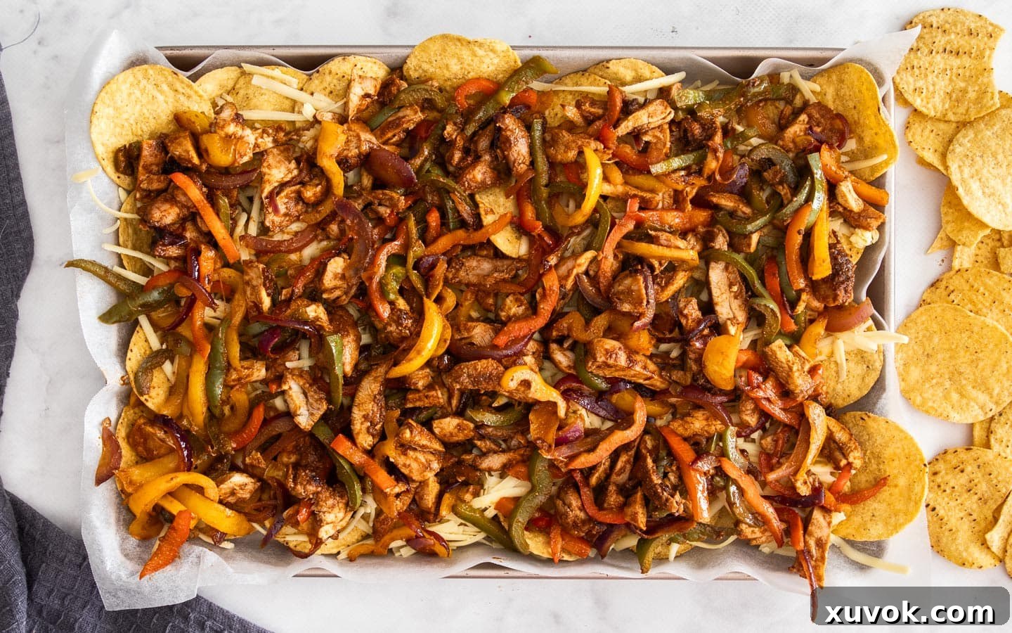 The corn chips topped with the chicken fajita mixture on a baking sheet.