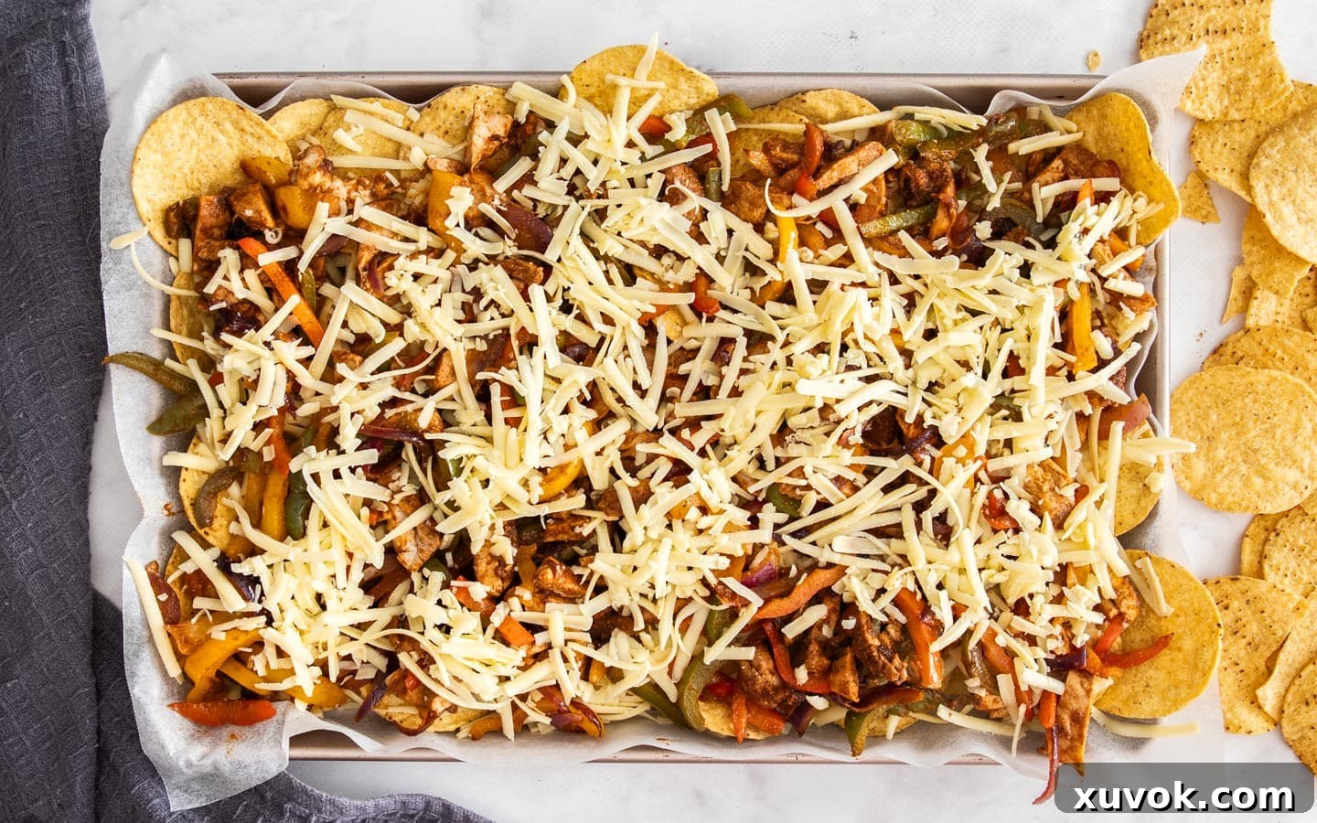 The nachos fully topped with cheese on a baking sheet, ready for the oven.