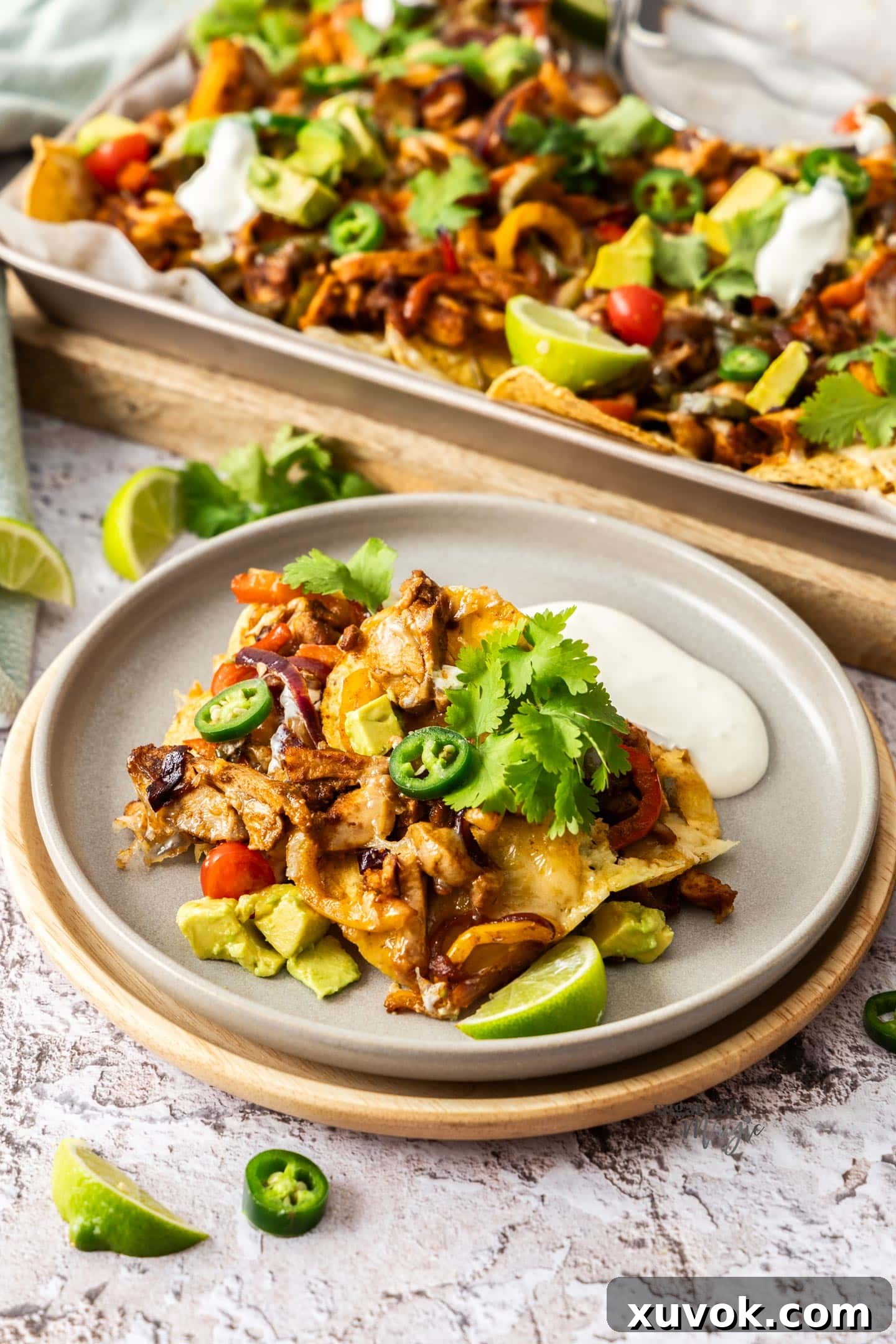 A serving of fajita chicken nachos on a dinner plate, garnished with a generous dollop of sour cream, avocado, and fresh cilantro.
