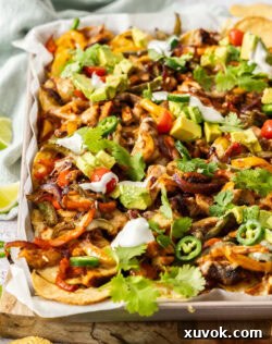 Chicken fajita nachos on a baking tray, topped with avocado slices and fresh coriander.