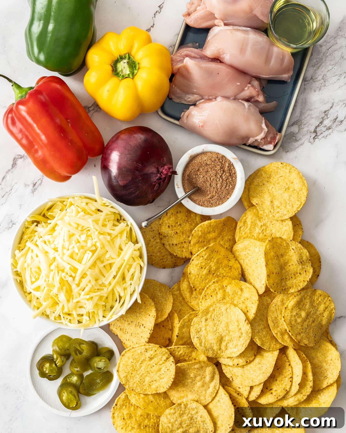 A selection of fresh ingredients laid out for making chicken fajita nachos, including chicken thighs, colorful bell peppers, red onion, and cheese.