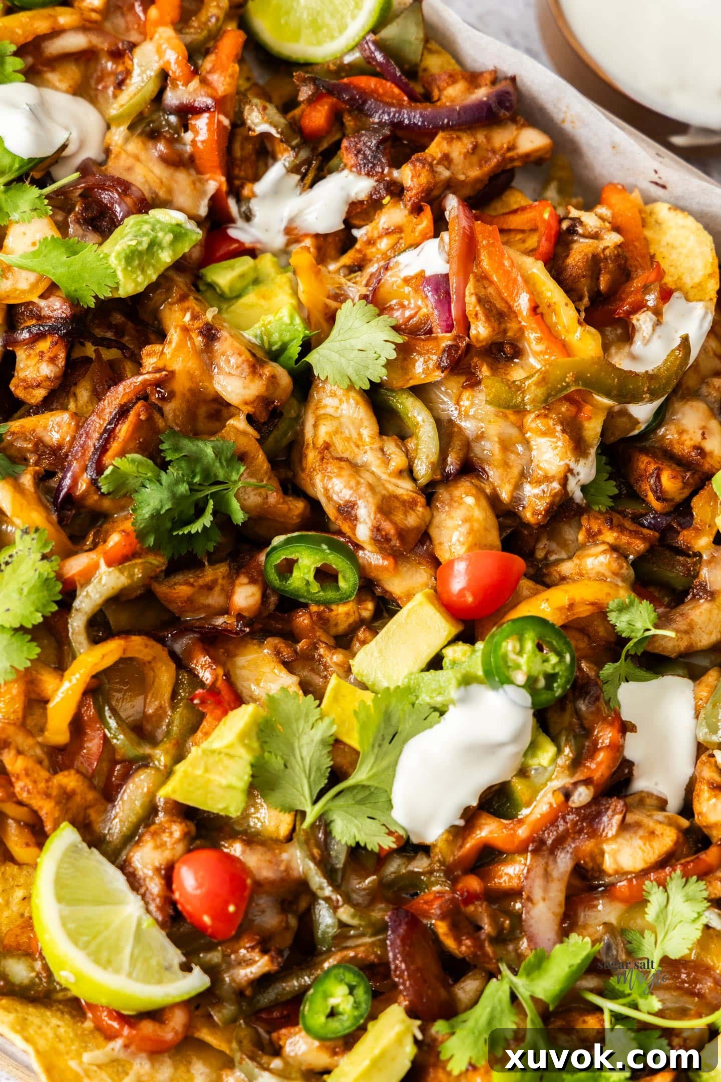 A close-up view of a serving of chicken fajita nachos, showcasing melted cheese, tender chicken, and colorful vegetables.