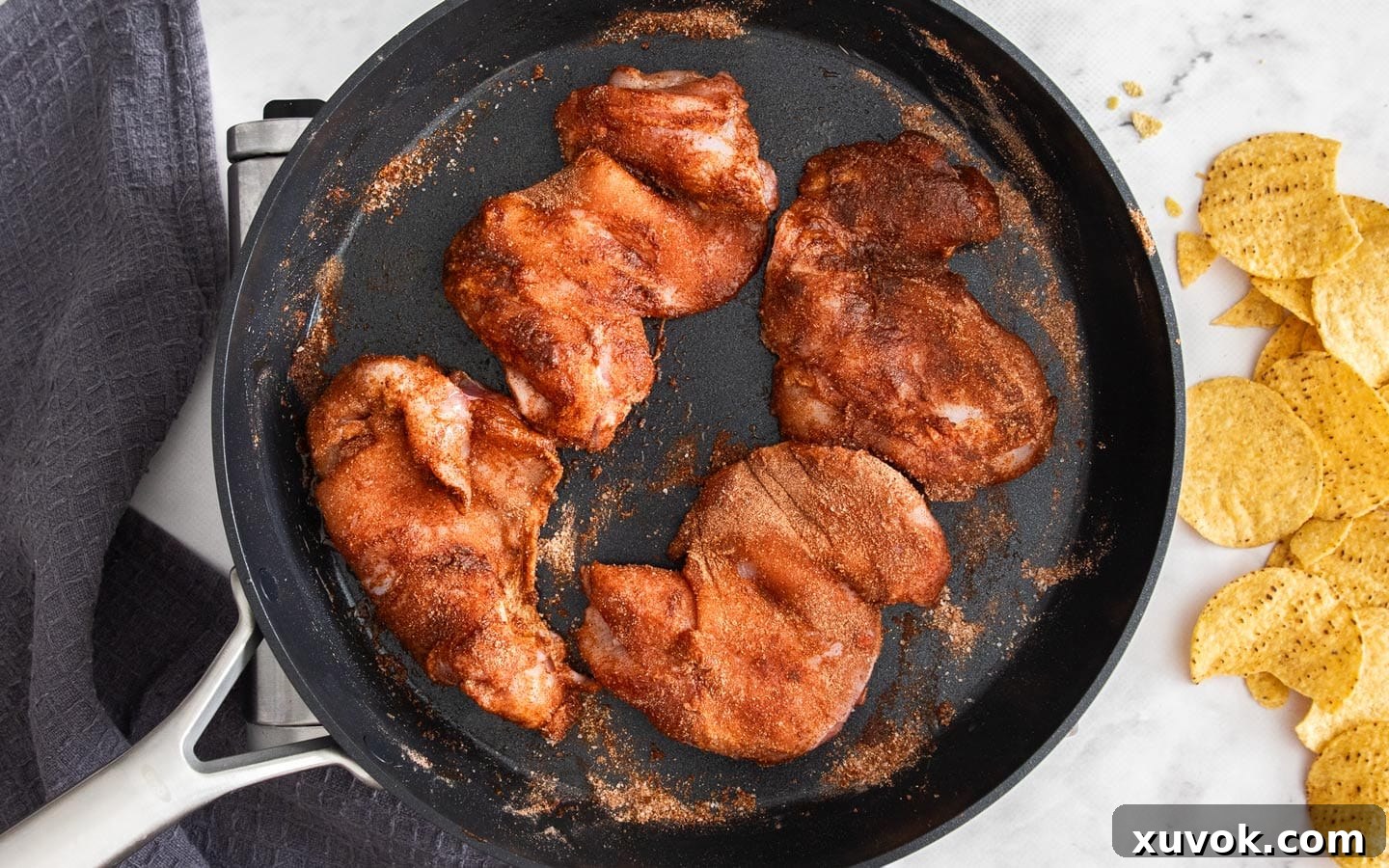 Seasoned chicken thighs being cooked in a pan, sizzling with spices.