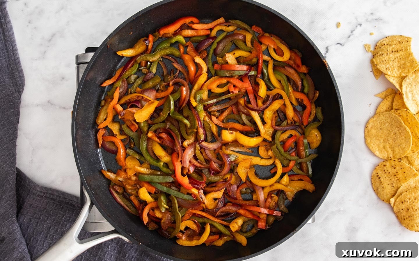 Sliced bell peppers, red onion, and pickled jalapenos softening in a pan.