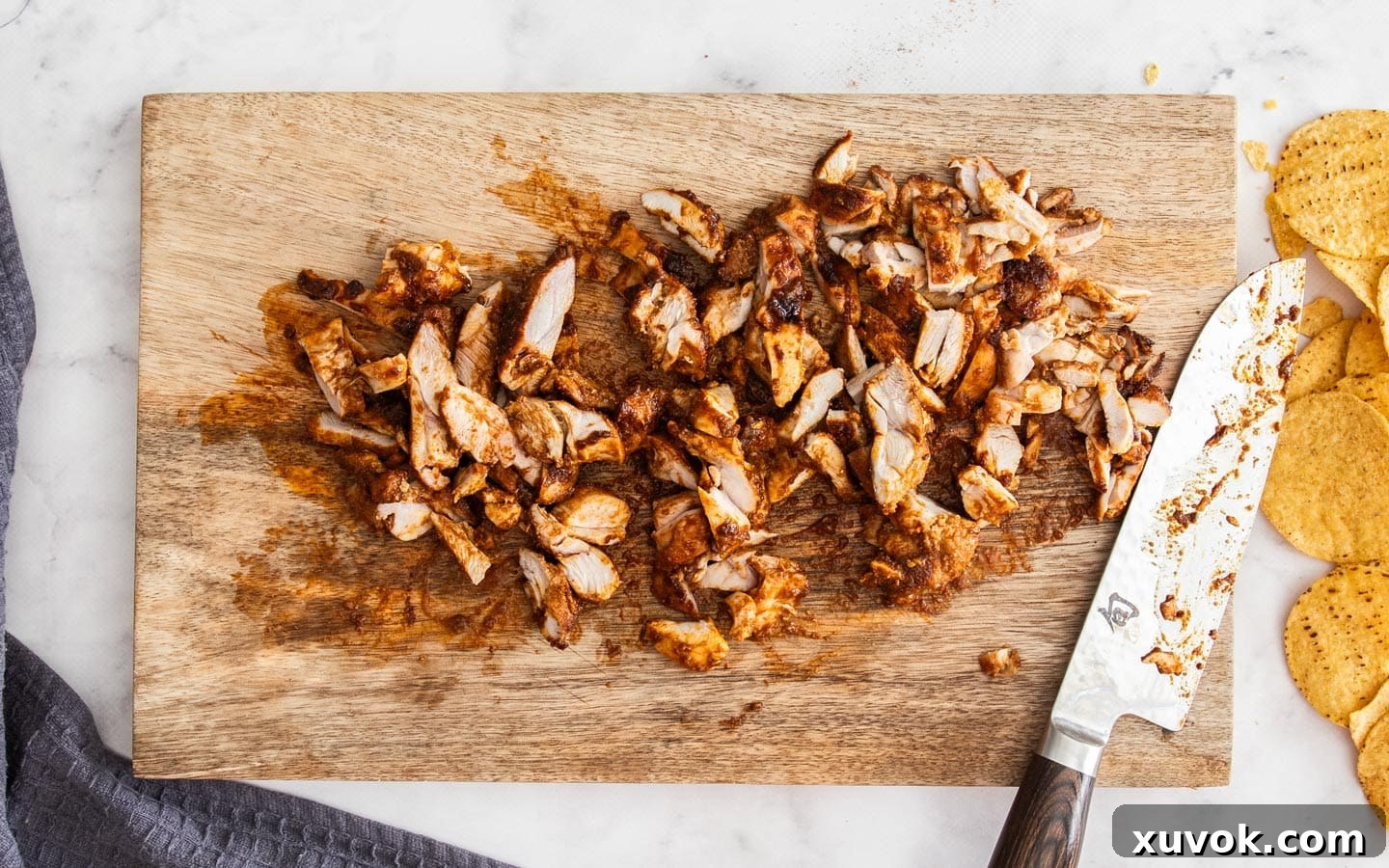 The cooked chicken sliced up into bite-sized pieces on a chopping board.