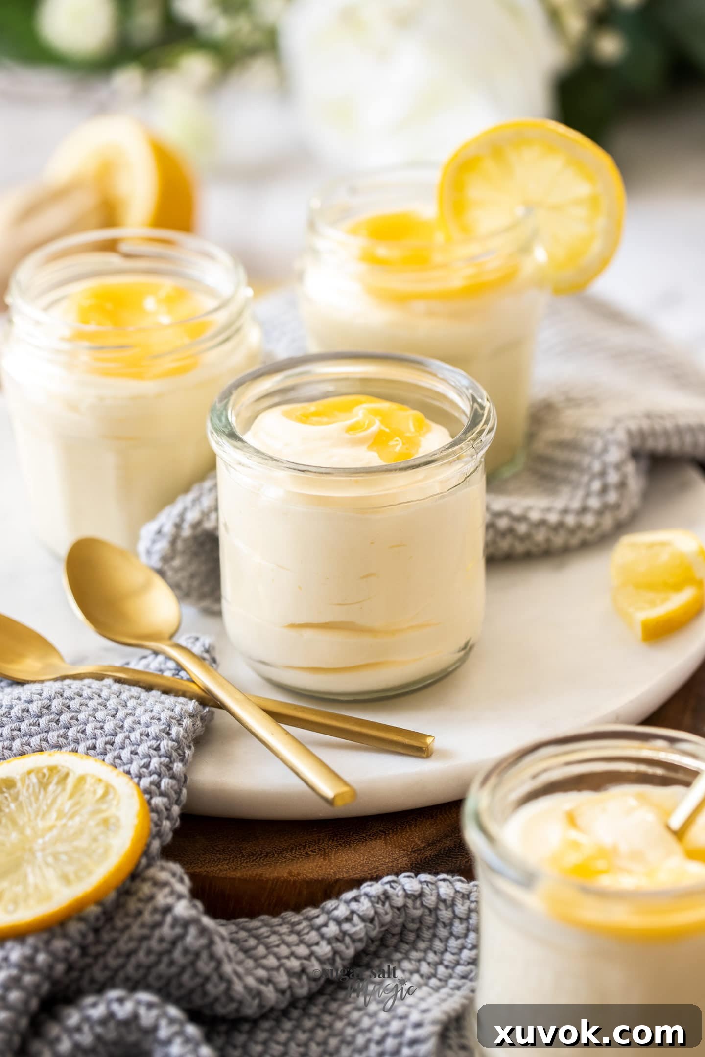 Four glasses elegantly filled with light yellow lemon curd mousse, each with a spoon resting in front, showcasing the dessert's creamy texture and inviting presentation.