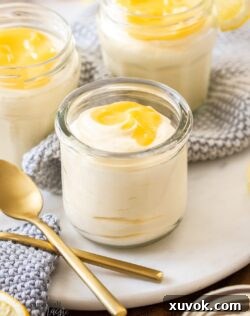 A glass filled with creamy lemon mousse topped with a swirl of extra lemon curd, with spoons elegantly placed nearby.