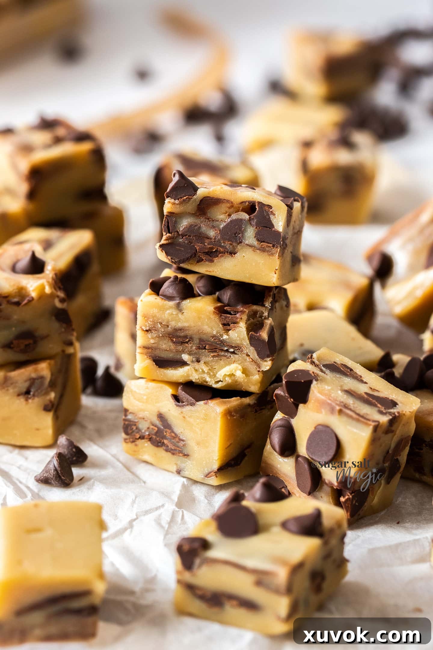 A stack of three squares of homemade Chocolate Chip Cookie Dough Fudge on baking paper, showcasing their perfect texture and generous chocolate chips, ready to be enjoyed.