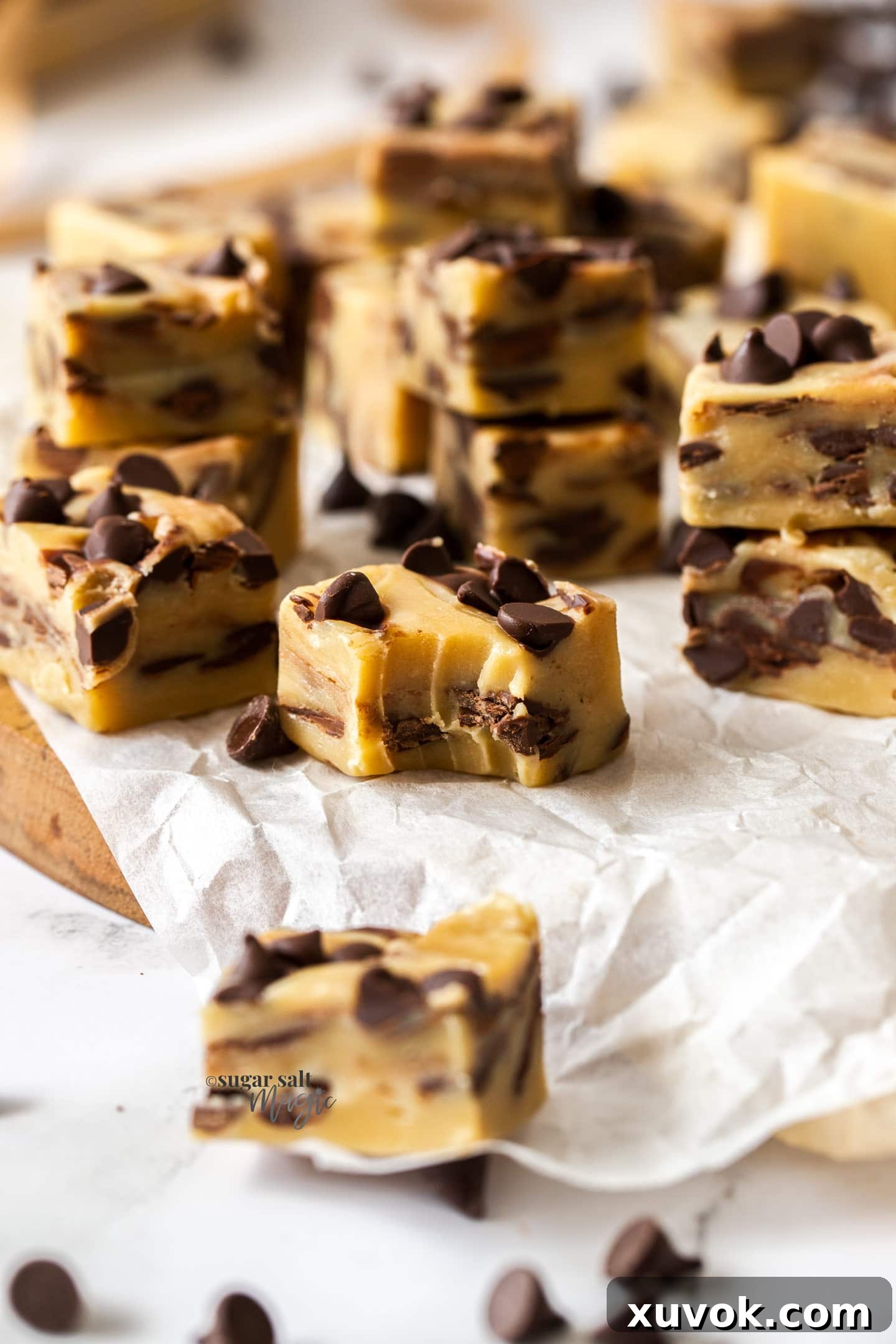 Several squares of homemade Chocolate Chip Cookie Dough Fudge on baking paper, with one piece showing a bite taken out, revealing its soft, creamy interior and embedded dark chocolate chips.