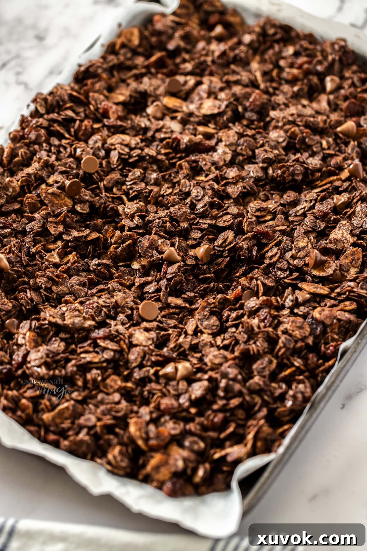 Close-up of freshly baked homemade chocolate granola scattered on a baking tray, showing crunchy clusters and chocolate chips.