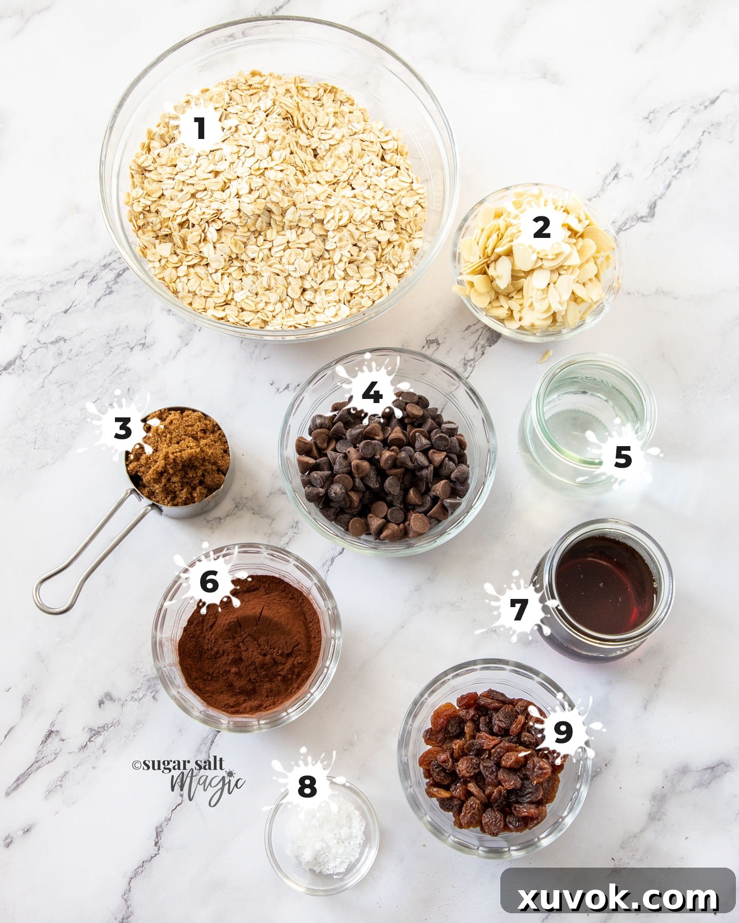 Various ingredients for chocolate granola, including oats, almonds, cocoa, and chocolate chips, neatly arranged on a marble countertop.