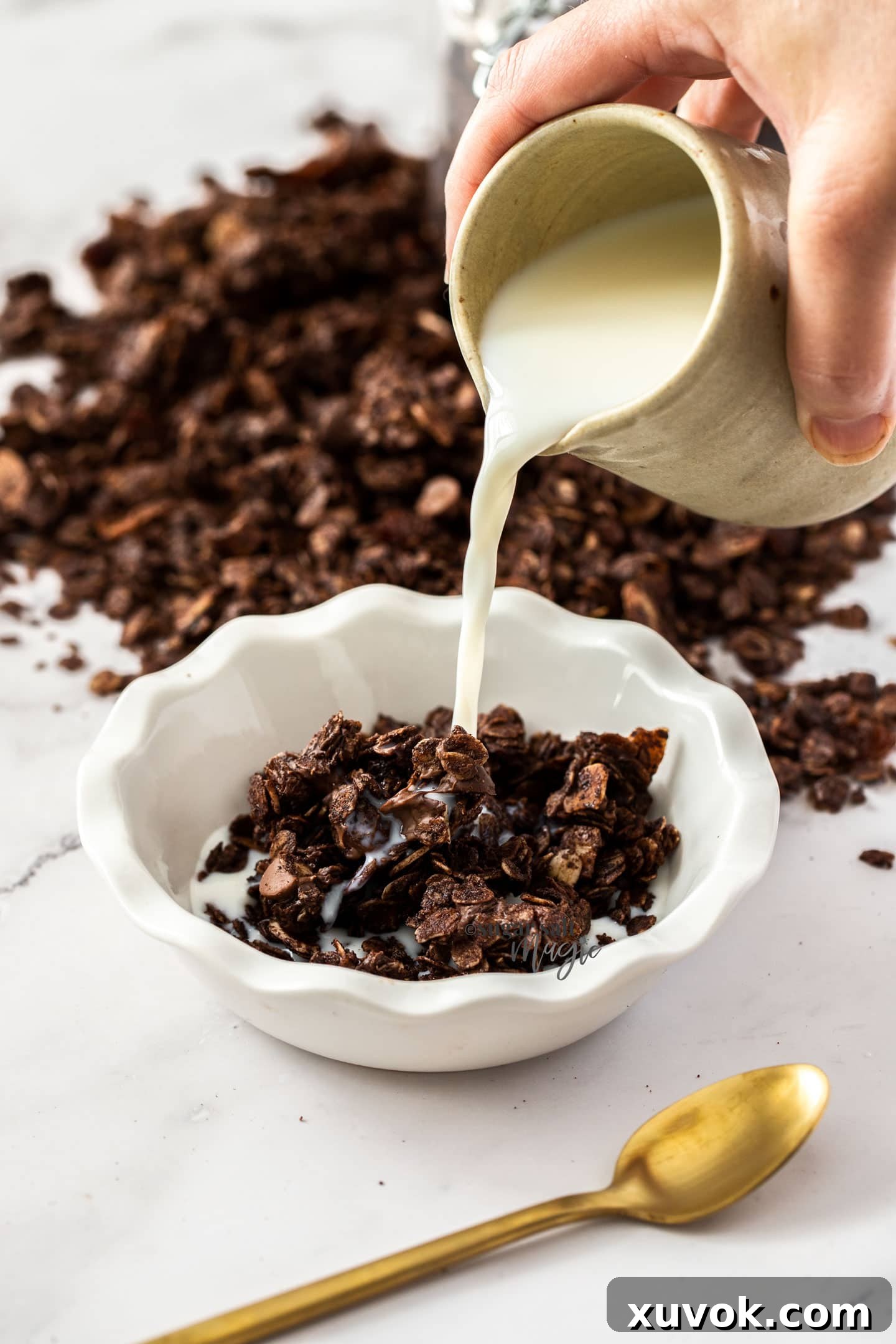 A stream of milk being poured over a bowl of homemade chocolate granola, ready to be enjoyed for breakfast.
