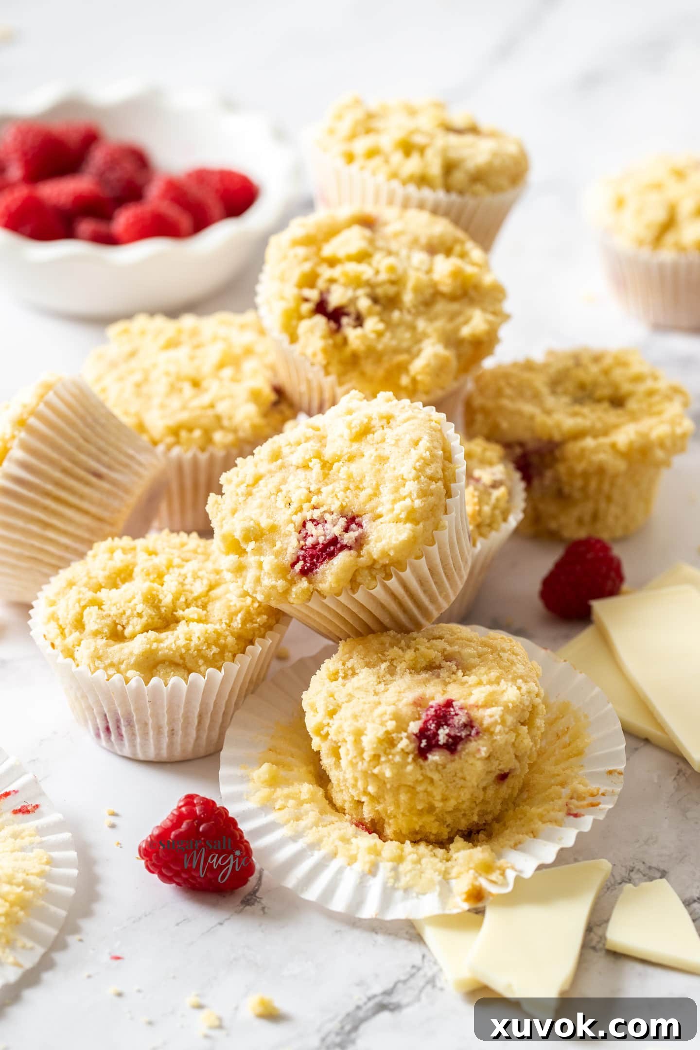 A batch of muffins with raspberries around them on a marble benchtop.