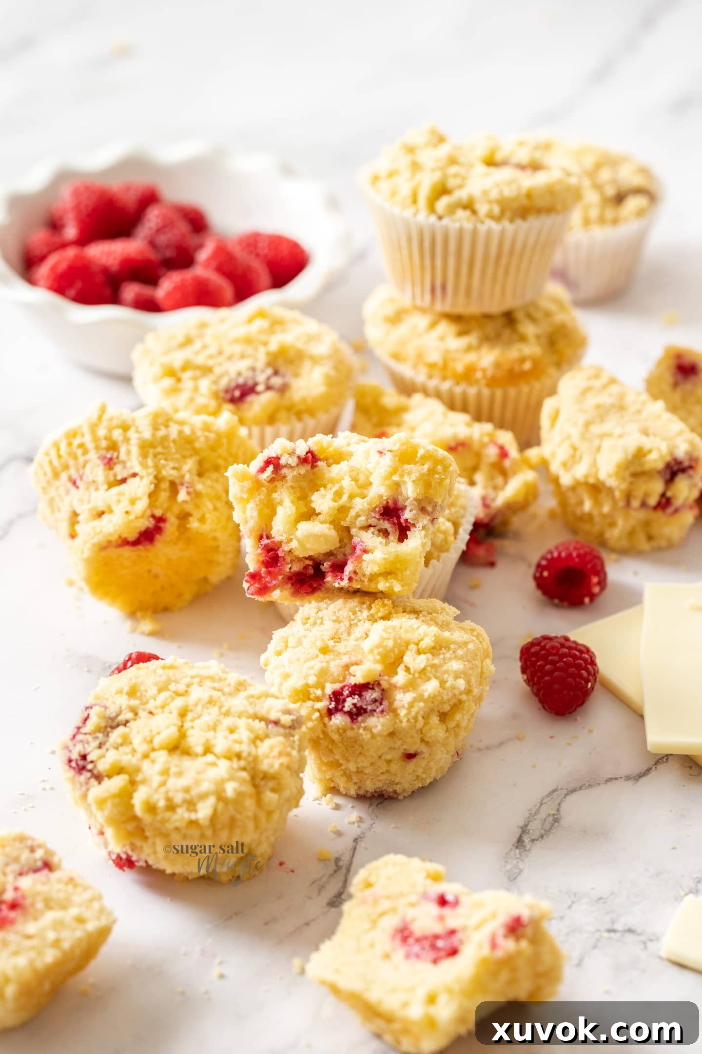 A batch of muffins with raspberries around them on a marble benchtop.