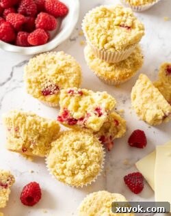 A batch of muffins with raspberries around them on a marble benchtop.