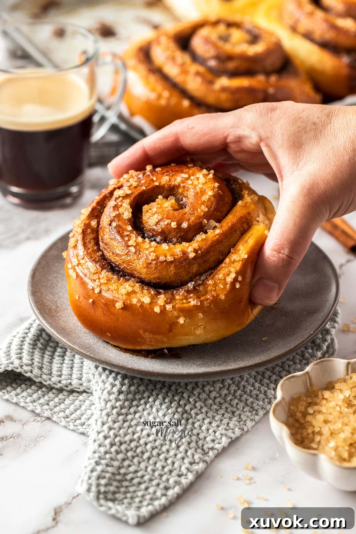 A hand lifting a freshly baked jumbo Swedish cinnamon bun off a grey plate, revealing its soft interior.