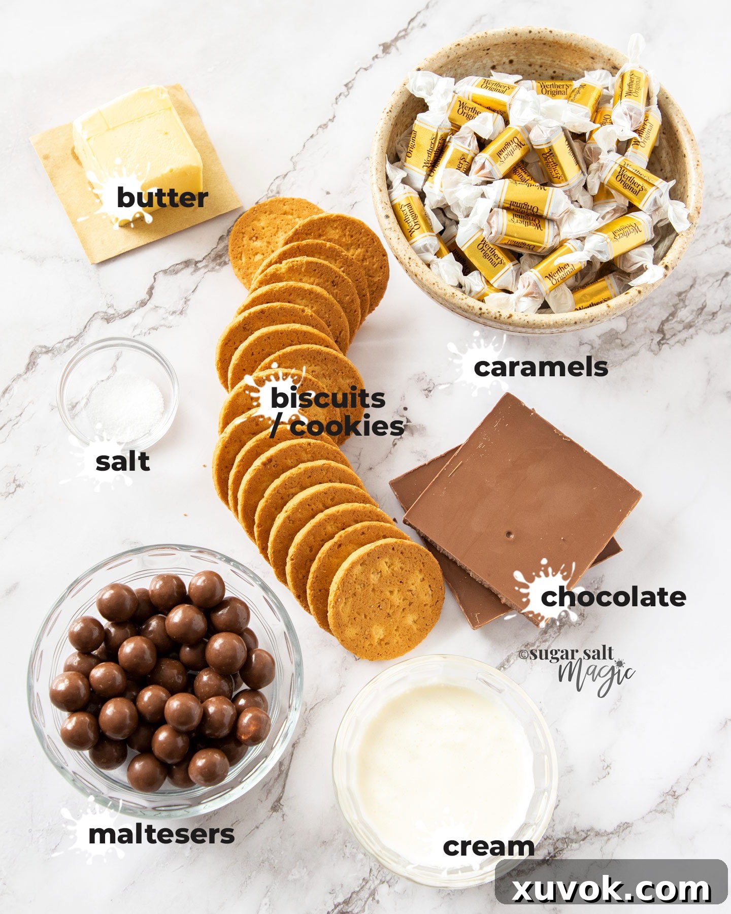 Assortment of ingredients for Caramel Malteser Slice laid out on a marble countertop, including biscuits, butter, caramels, cream, Maltesers, and chocolate.