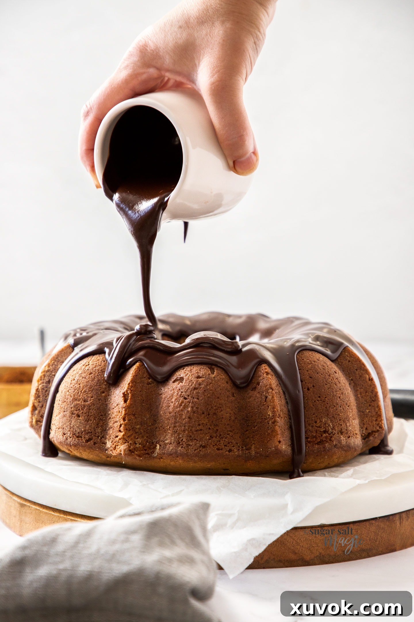 Silky chocolate ganache being skillfully poured over a freshly baked, intricately designed bundt cake, creating a tempting glaze.