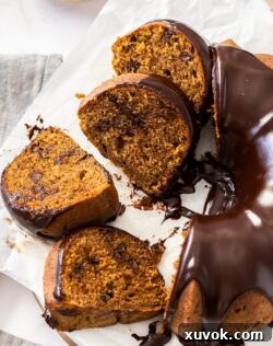 A chocolate coffee bundt cake covered in rich ganache with several slices on a white serving plate.