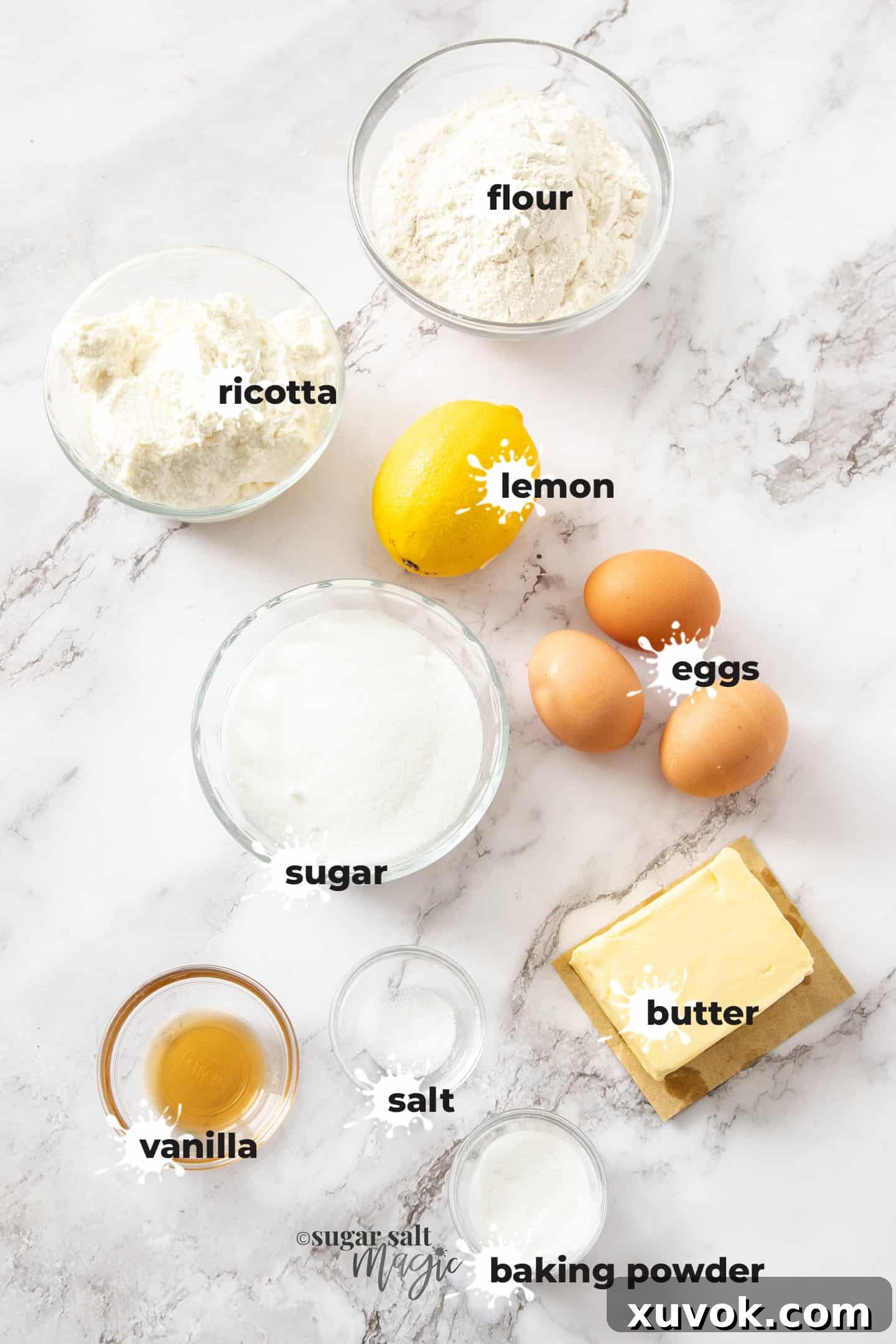 A vibrant flat lay of ingredients for lemon ricotta cake meticulously arranged on a clean white marble benchtop. Items include lemons, eggs, a block of butter, a bowl of ricotta, flour, sugar, baking powder, and vanilla extract.
