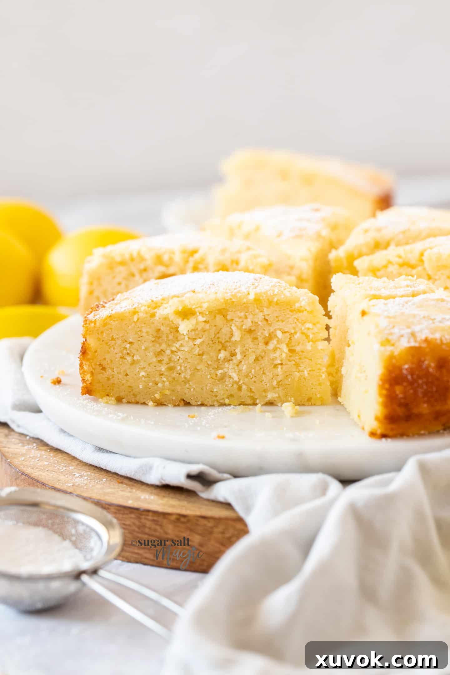 A single, perfectly sliced piece of lemon ricotta cake resting elegantly on a pristine white marble platter, highlighting its moist and creamy texture. The background is softly blurred, focusing attention on the cake.