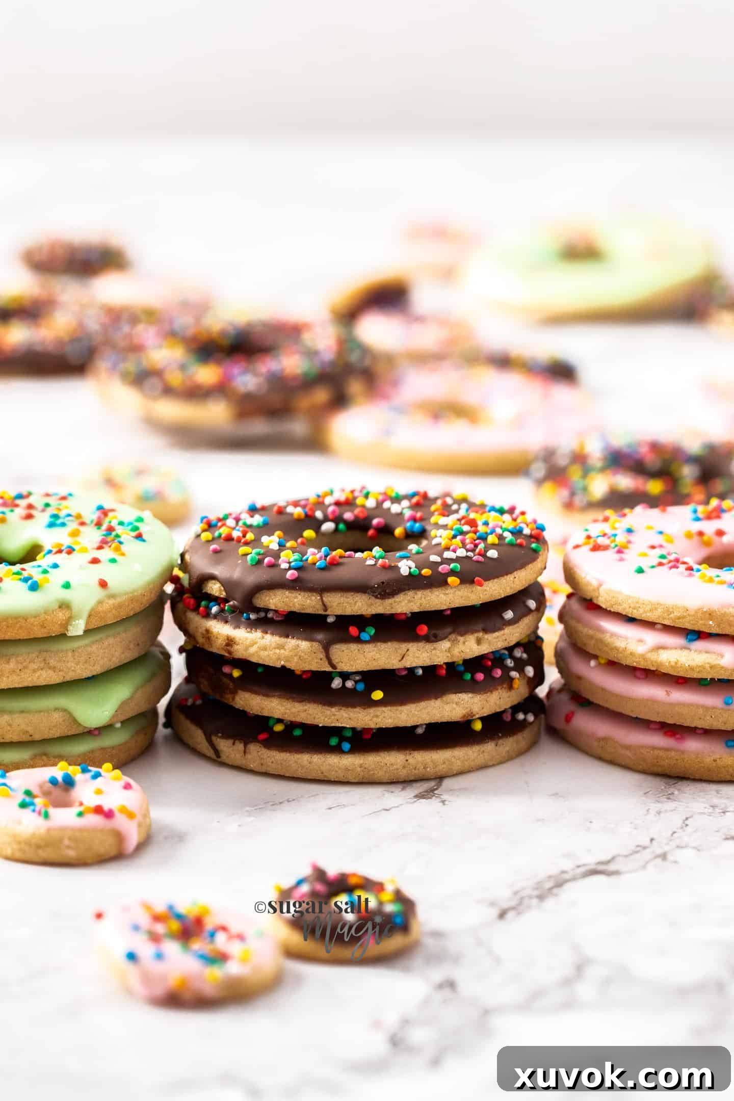A beautiful stack of four chocolate-coated donut cookies adorned with sprinkles, flanked by two other stacks on a marble surface, highlighting their festive appeal.