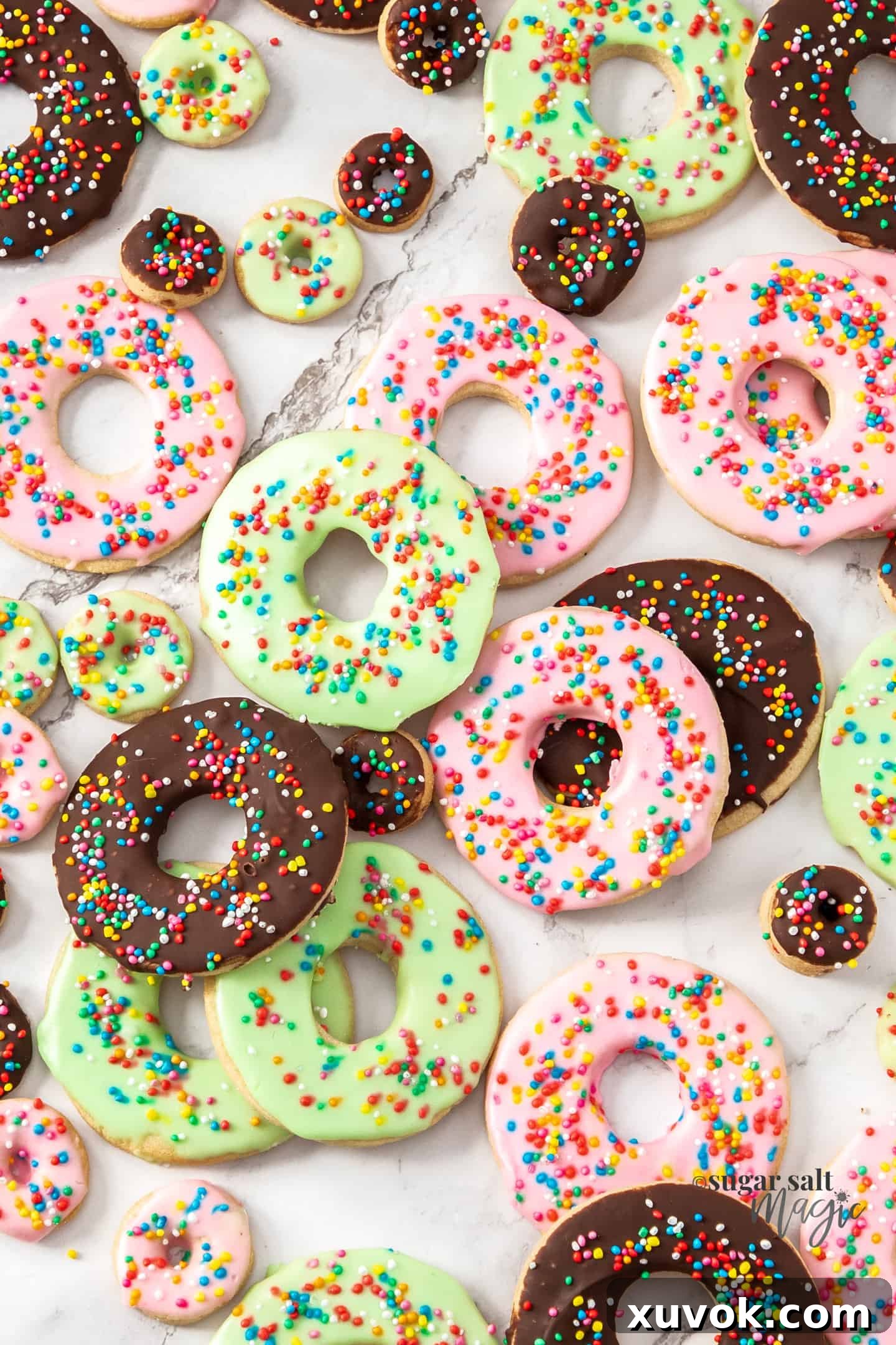 A large batch of freshly baked and decorated donut sugar cookies arranged artfully on a marble surface, showcasing their delicious appeal.