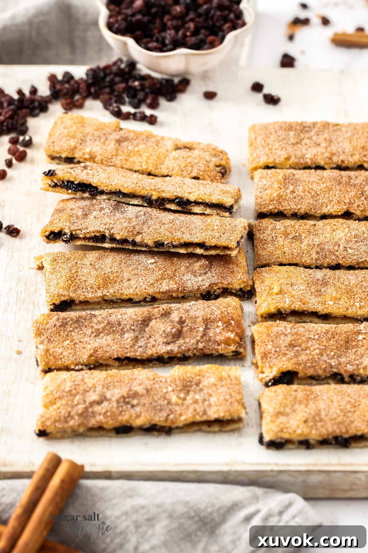 A beautifully arranged line of rectangular Garibaldi biscuits, showcasing their golden-brown edges and generous currant filling, on a pristine white board. Perfect for a tea break.