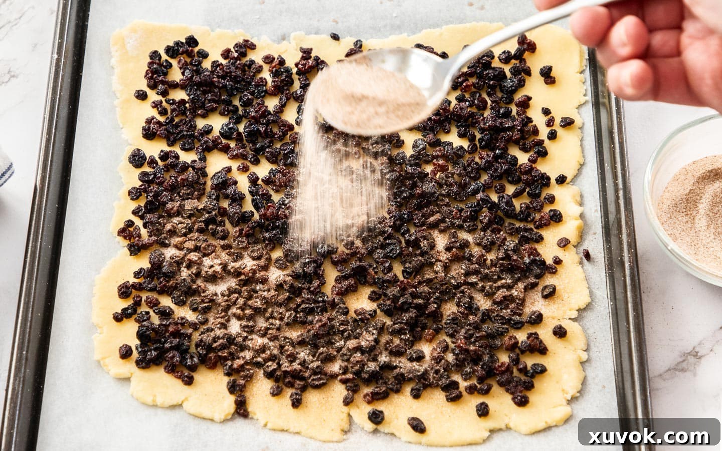The first layer of biscuit dough, rolled out into a neat square, generously covered with plump, rehydrated currants and a dusting of cinnamon sugar.