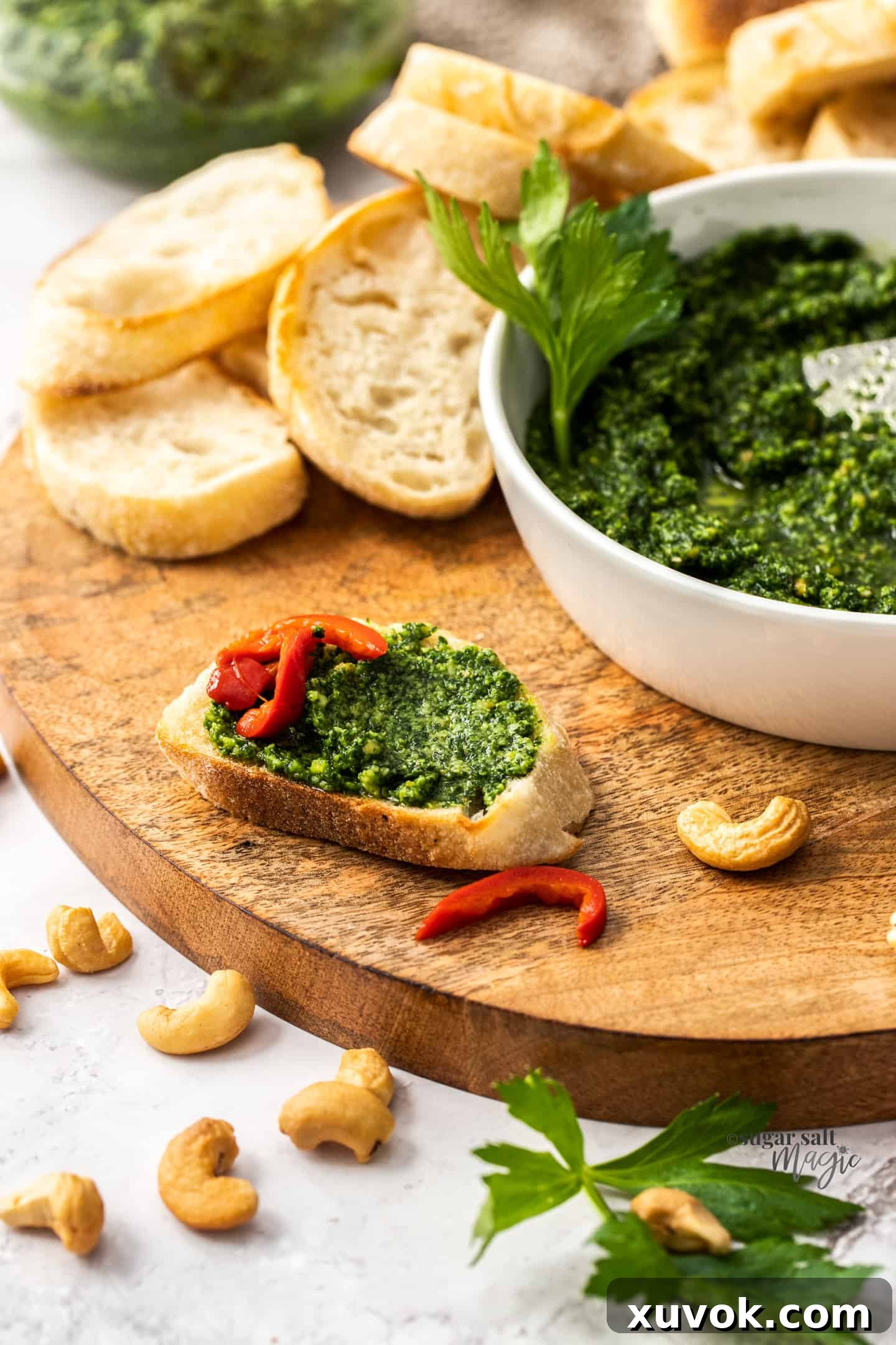 A small, toasted slice of baguette generously spread with bright green celery leaf pesto, ready to be enjoyed.