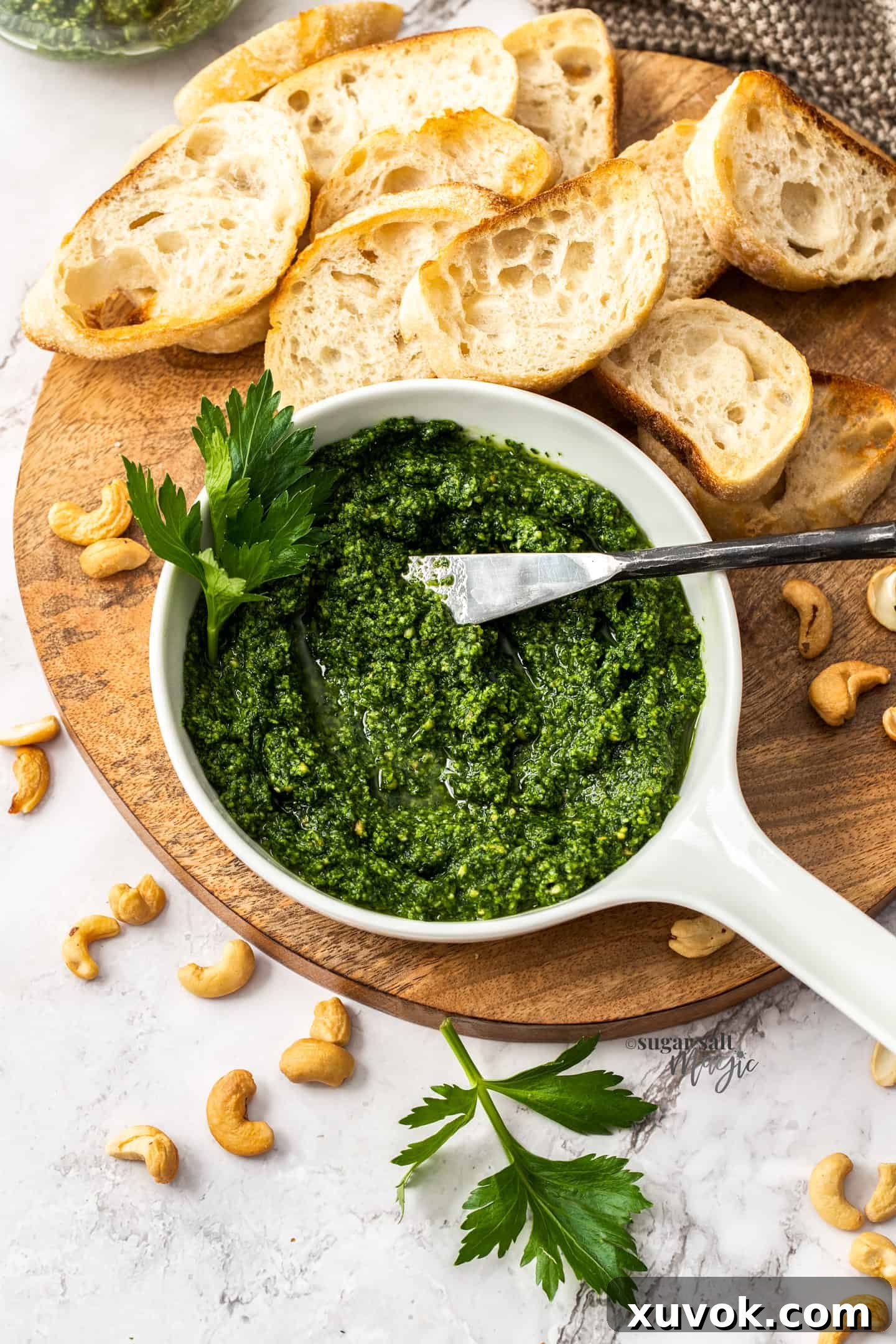 A white bowl brimming with vibrant green celery leaf pesto, accompanied by several slices of crusty bread on a wooden board, inviting you to dip.
