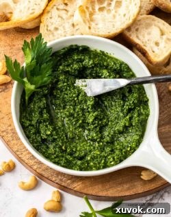 A white bowl filled with green pesto on a wooden board.