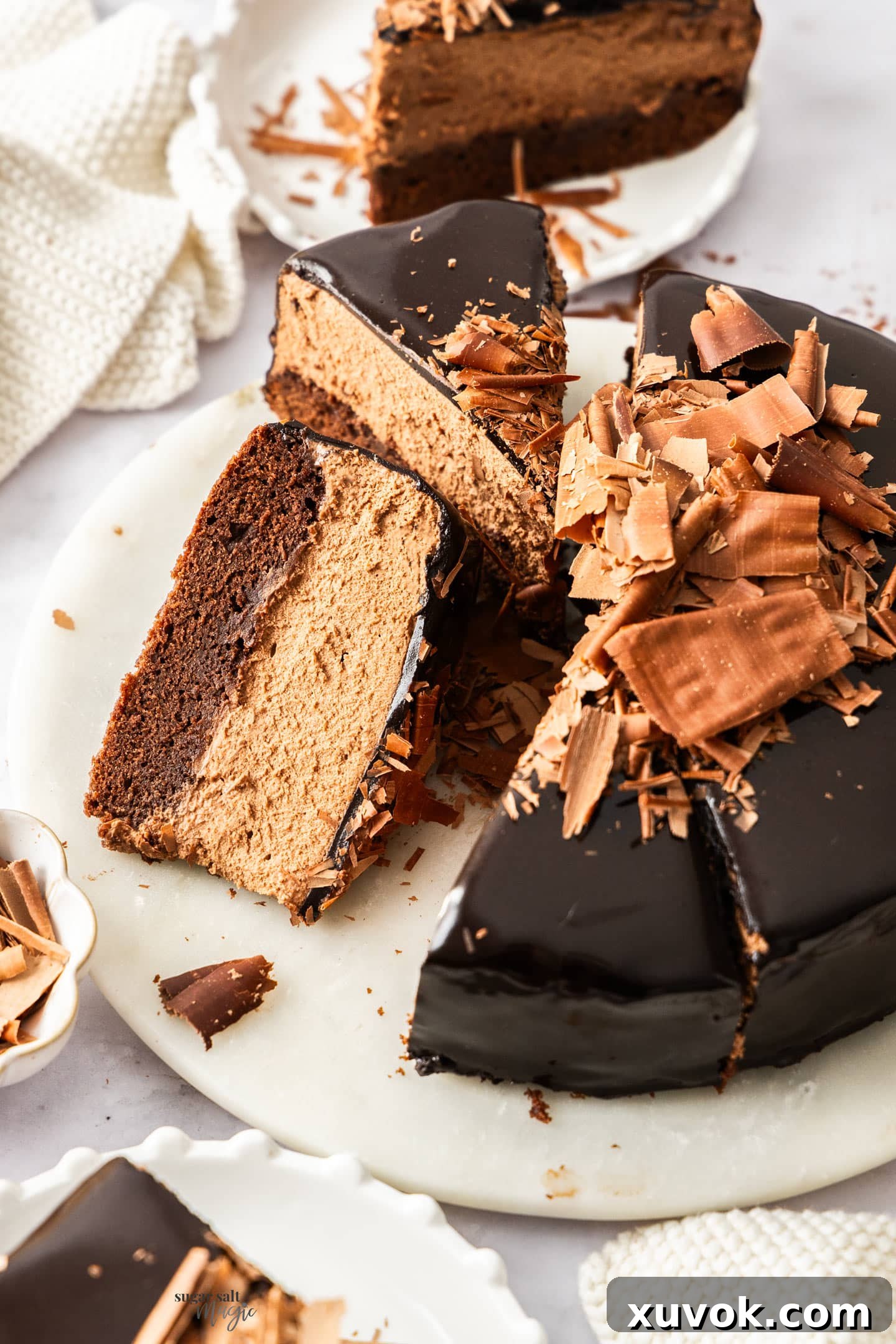 A chocolate mousse cake on a marble platter, cut into slices with one on it's side.