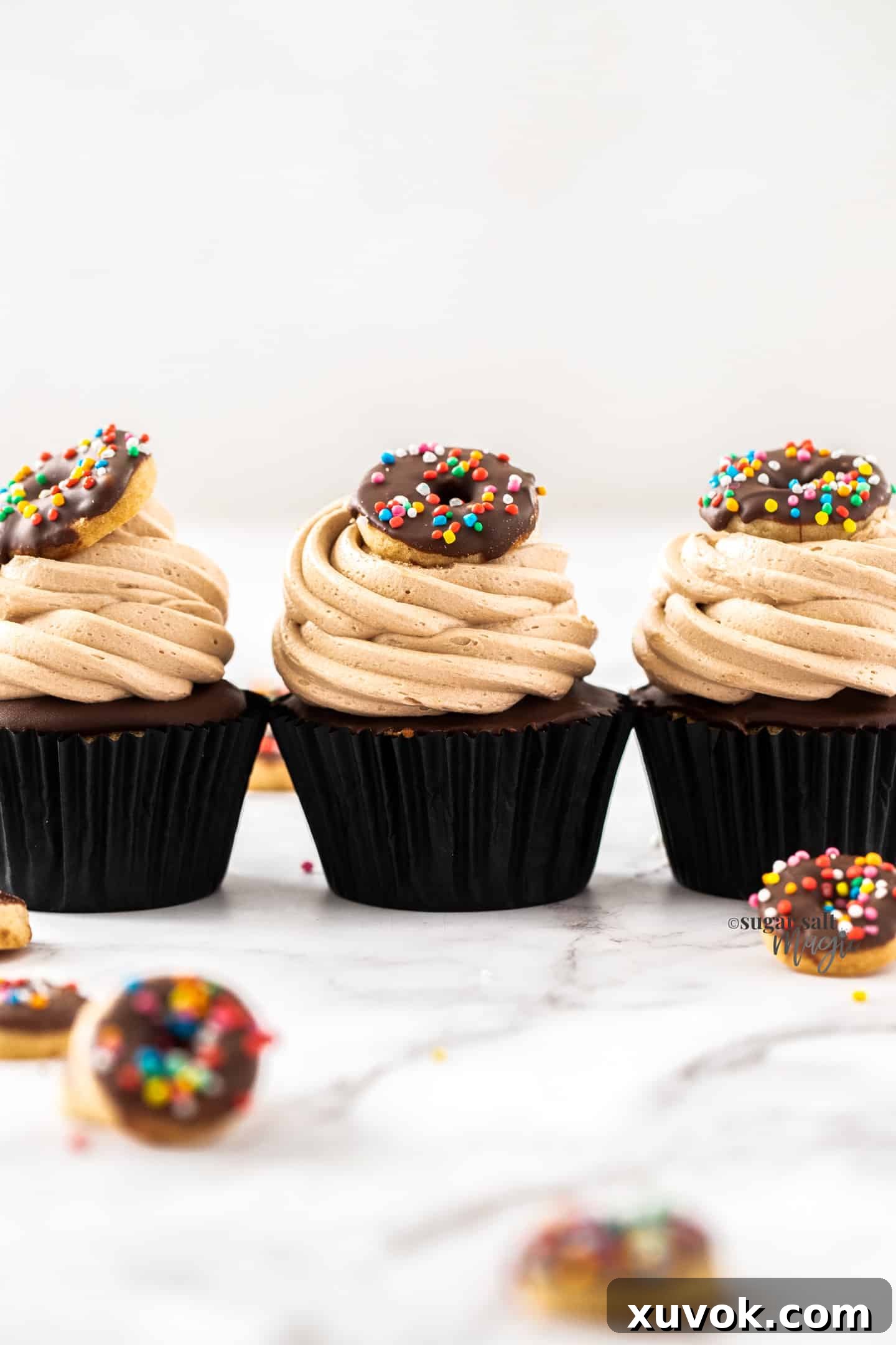 Three beautifully frosted chocolate donut cupcakes, lined up elegantly, showcasing their rich chocolate swirls and fluffy texture.