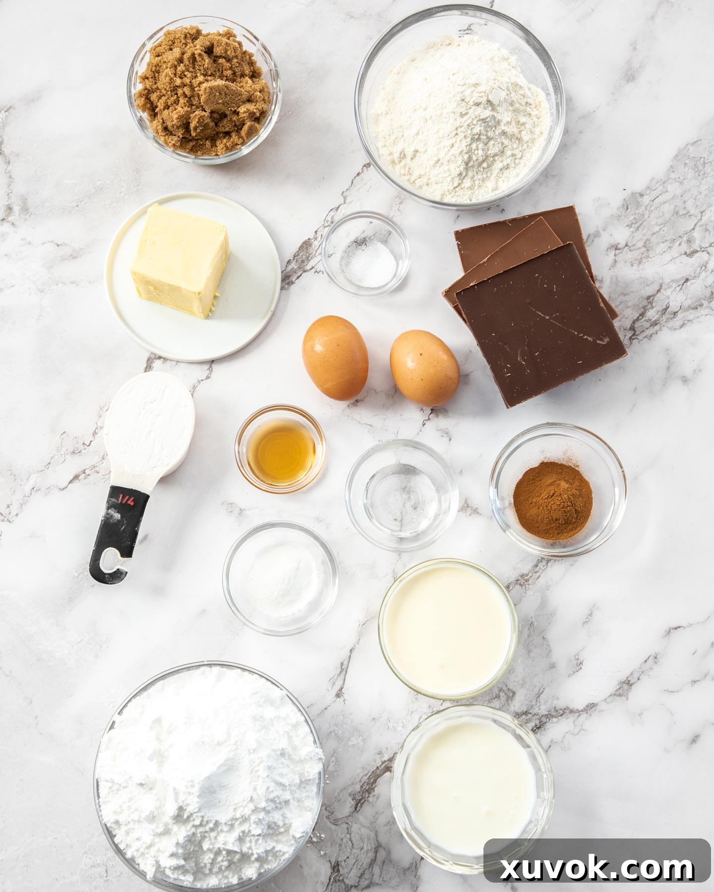 A flat lay photograph showcasing all the ingredients required for making chocolate donut cupcakes, neatly arranged on a pristine marble surface.