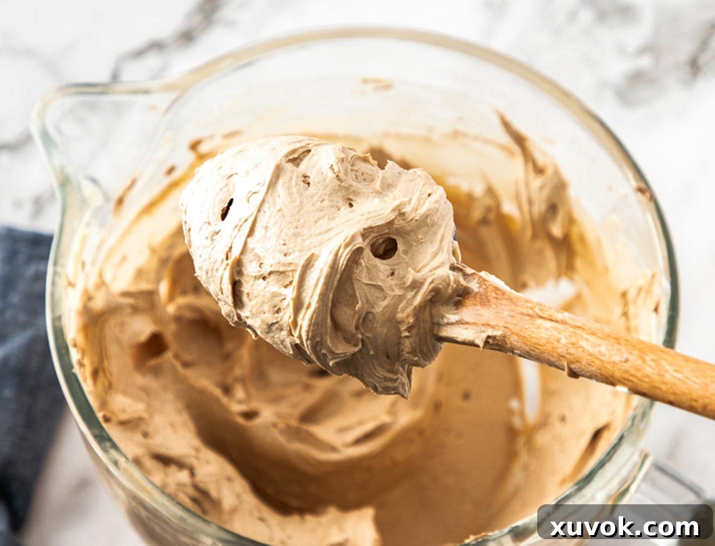 A spoonful of rich, airy, and perfectly whipped chocolate frosting being lifted from a mixing bowl, showcasing its beautiful texture.
