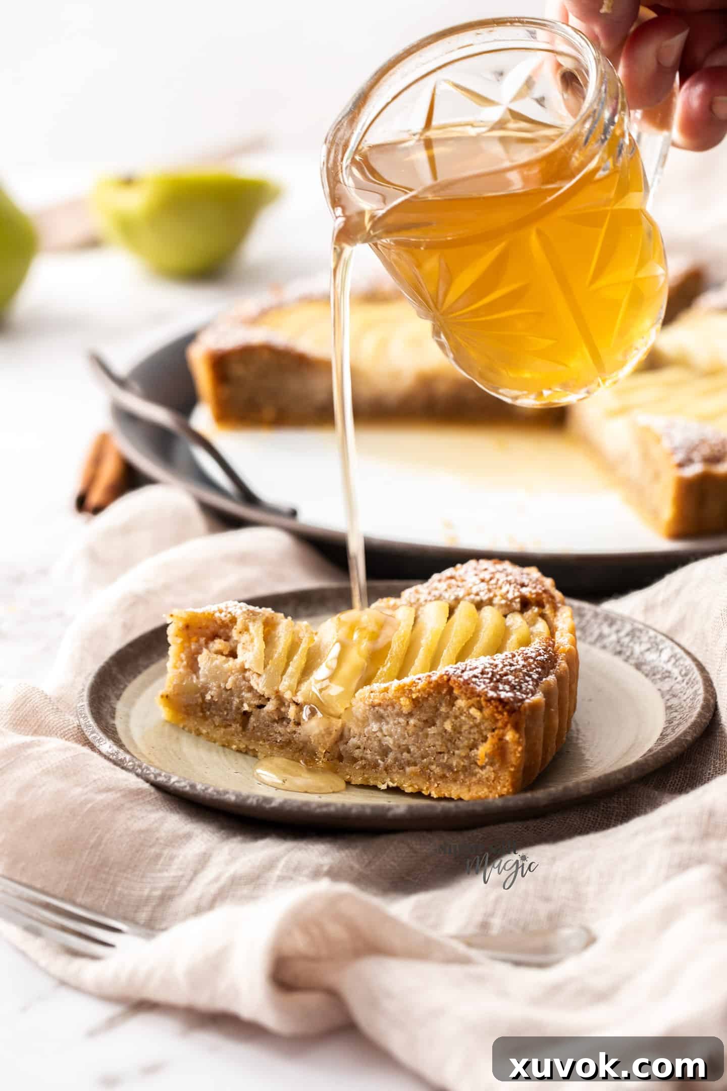 Syrup being poured onto a slice of pear tart from a small glass jug.