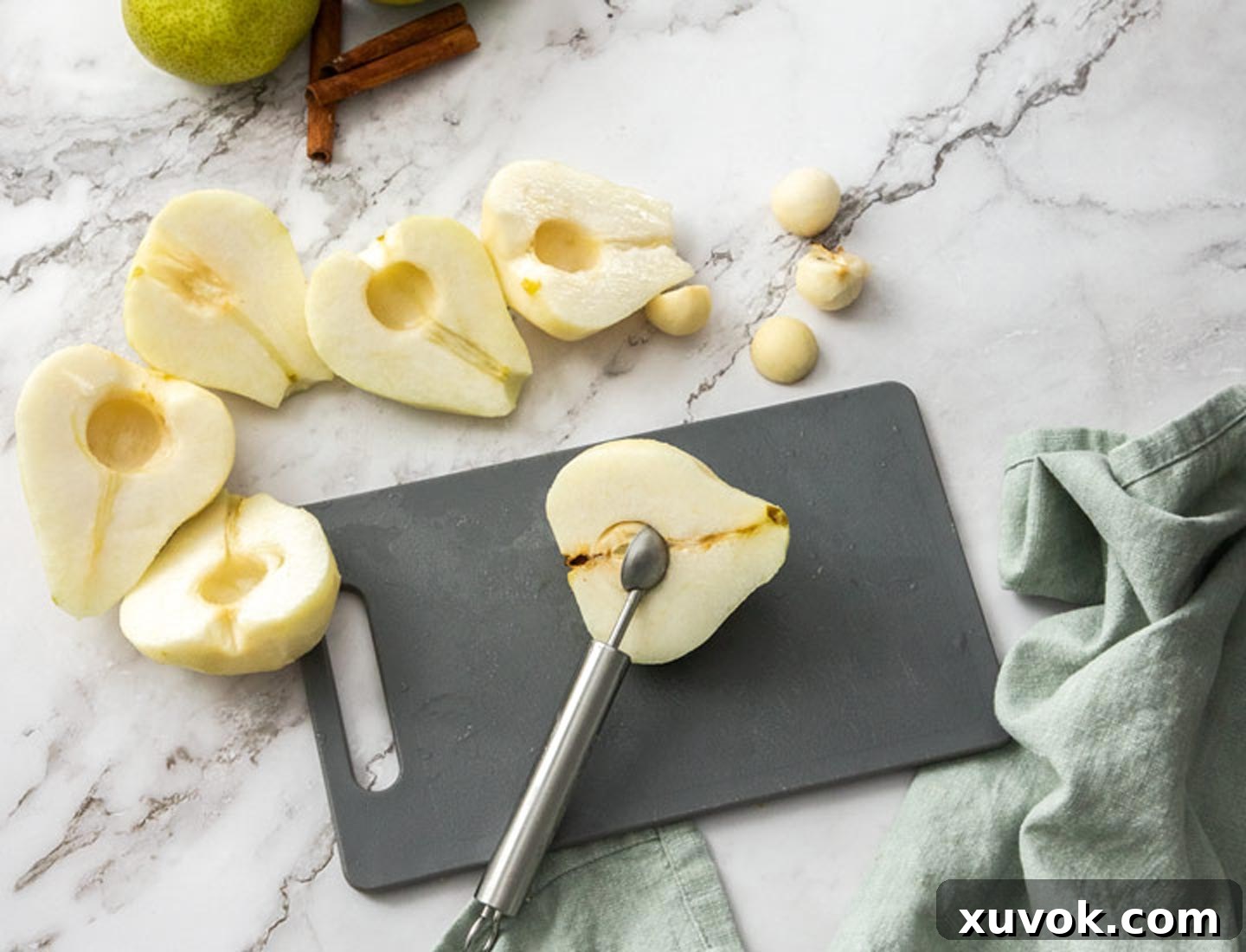 The pears being cored with a melon baller on a chopping board.