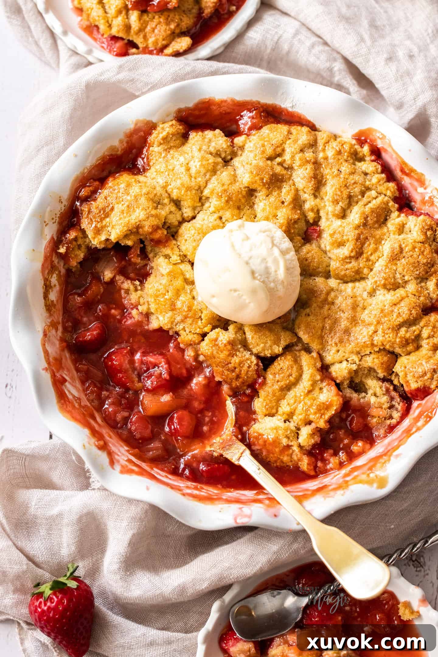 A white pie dish filled with strawberry rhubarb cobbler and a scoop of ice cream.