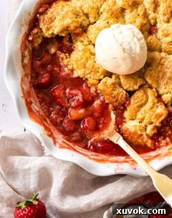 A white pie dish filled with strawberry rhubarb cobbler and a scoop of ice cream.