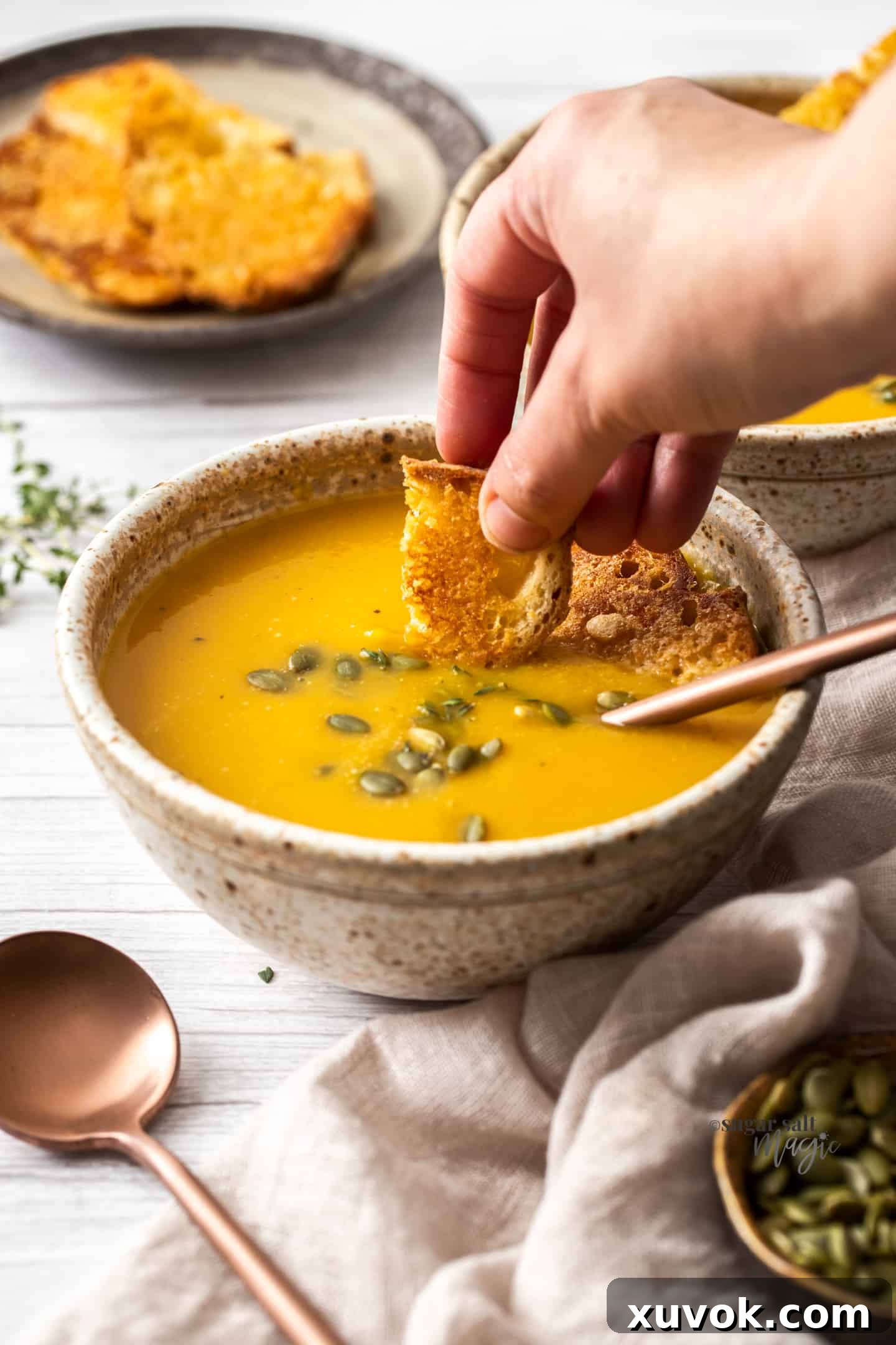 A hand gently dipping a piece of crusty bread into a bowl of creamy butternut squash soup, highlighting the inviting texture and warmth of the dish.