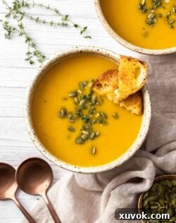 Top down view of a bowl filled with butternut squash soup topped with crusty bread and pepitas, inviting and warm.