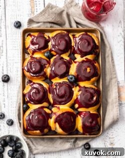 Glazed cinnamon rolls still in the baking tin on a white wooden surface, highlighting their homemade charm and readiness for serving.